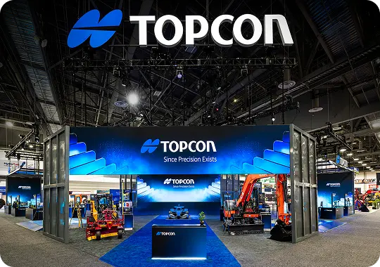 TOPCON precision-equipment trade show booth with overhead truss signage and product displays