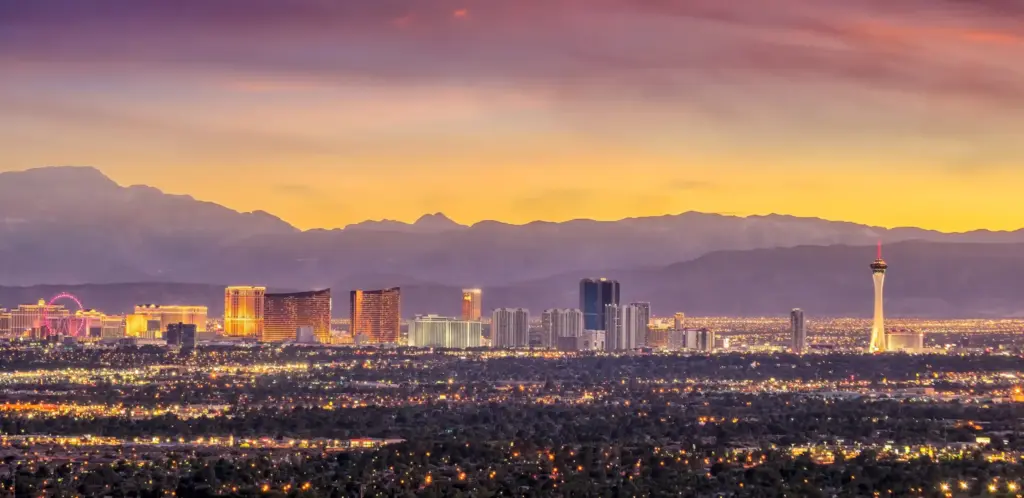 Las Vegas skyline at sunset with the Strip resorts and distant mountains under a purple and orange sky