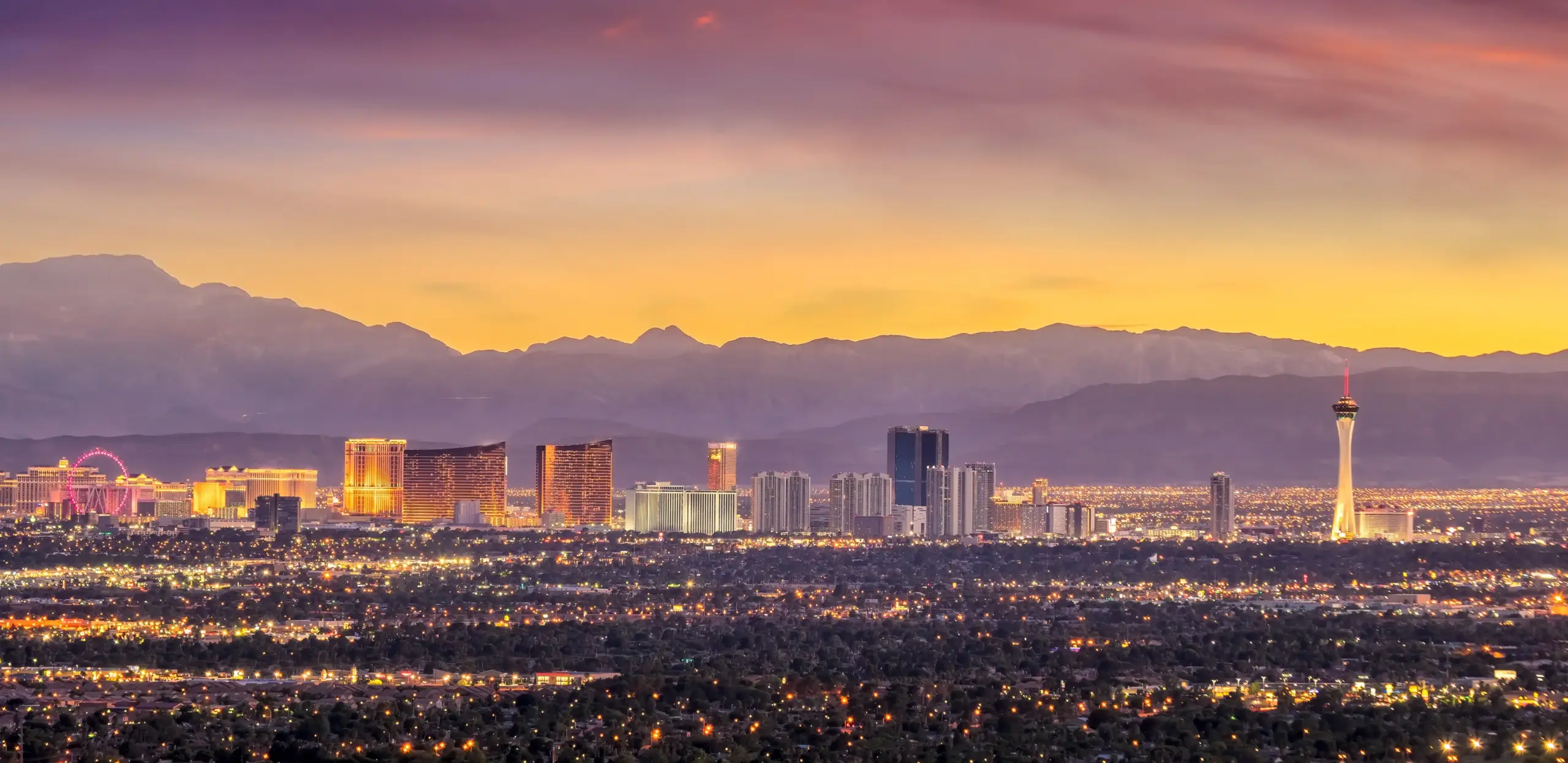 Las Vegas skyline at sunset with the Strip resorts and distant mountains under a purple and orange sky